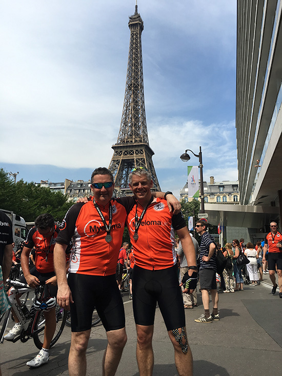 Marcus Maisey and Gary Cretton wearing orange Myeloma UK t-shirts and medals standing in front of the Eiffel Tower