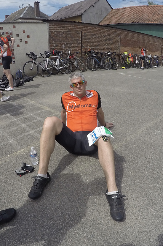 Gary Cretton sitting on the floor wearing orange myeloma UK t-shirt with an ice pack on his knee